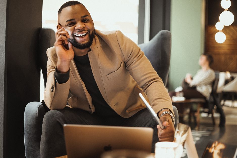 Businessman sitting in a cafe, enjoying a phone call with a laptop nearby.