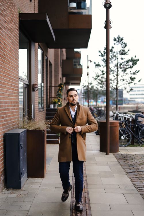 Free A man in a coat walks confidently down a stylish street in Copenhagen, showcasing urban fashion. Stock Photo