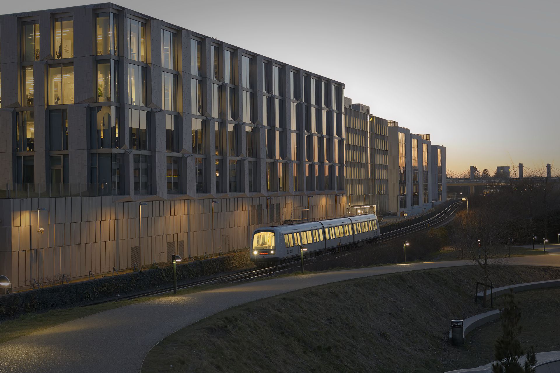 A modern urban train passing through Frederiksberg, Denmark at dusk with illuminated buildings.