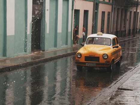Yellow classic taxi driving through a wet street on a rainy day, capturing urban life.