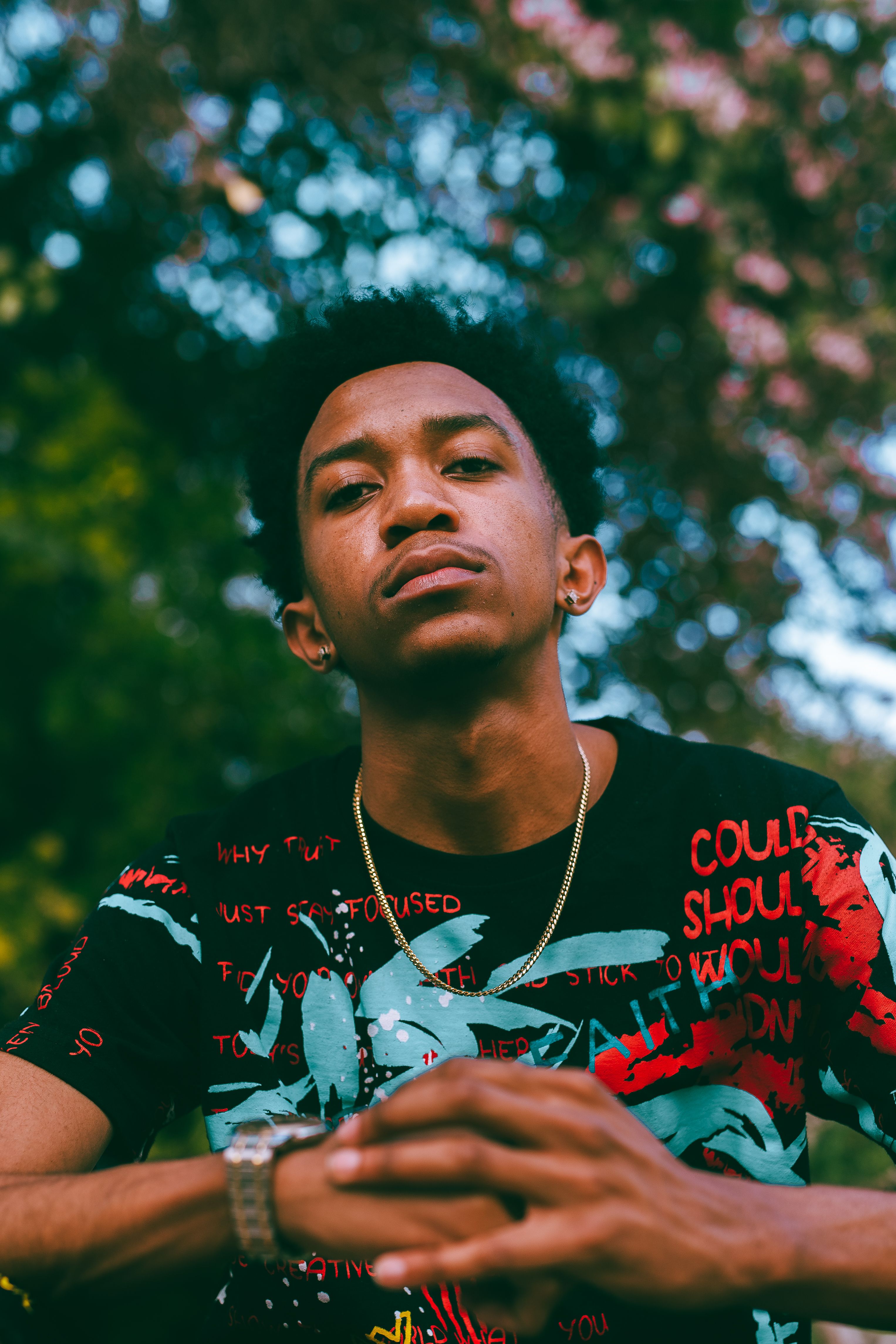 A stylish young man poses confidently outdoors with hands together, exuding modern elegance.