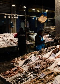 Bustling indoor fish market with fresh seafood and vendors under warm lighting.