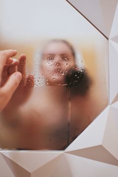 Close-up of an artistic hand touching a steamed mirror, capturing reflection and water droplets.