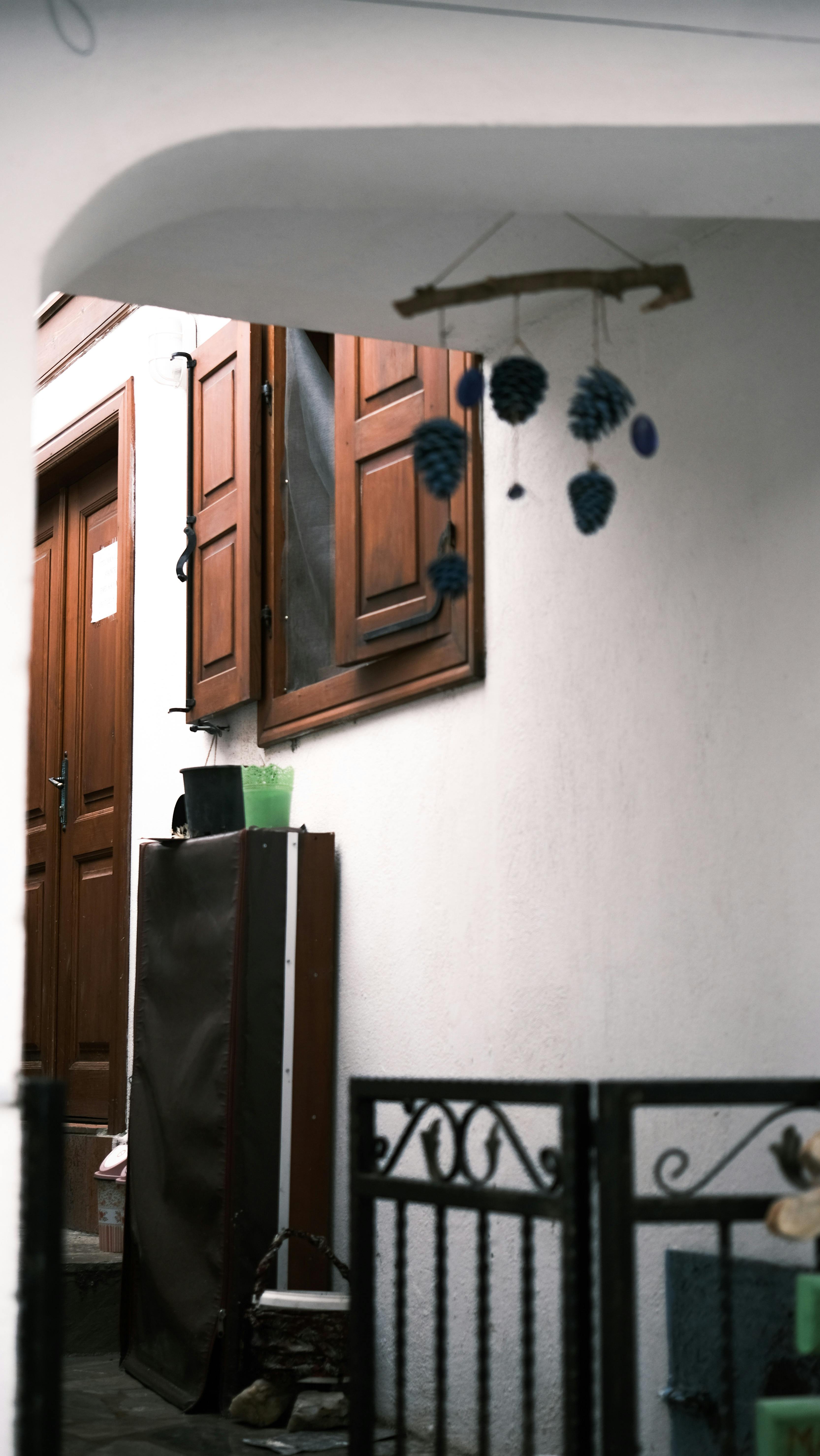 A rustic courtyard with wooden shutters, white walls, and a decorative hanging mobile.