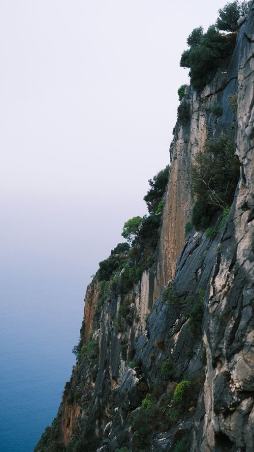 Free A striking photograph capturing a rocky cliffside with lush greenery overlooking a calm ocean. Stock Photo