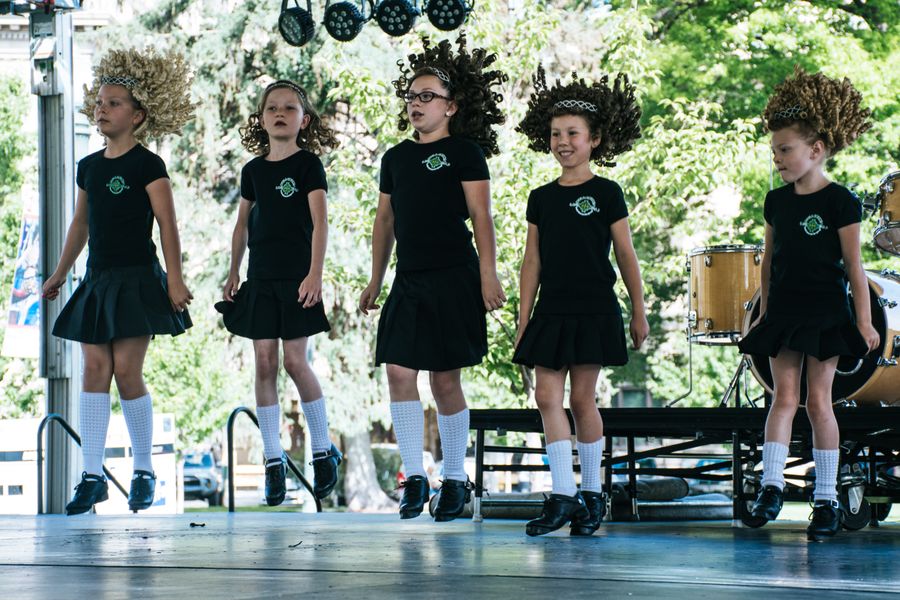 Young girls showcasing Irish dance on an outdoor stage, wearing wigs and traditional attire
