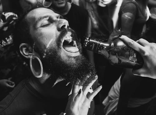 Person Holding Bottle in Front of Man's Mouth