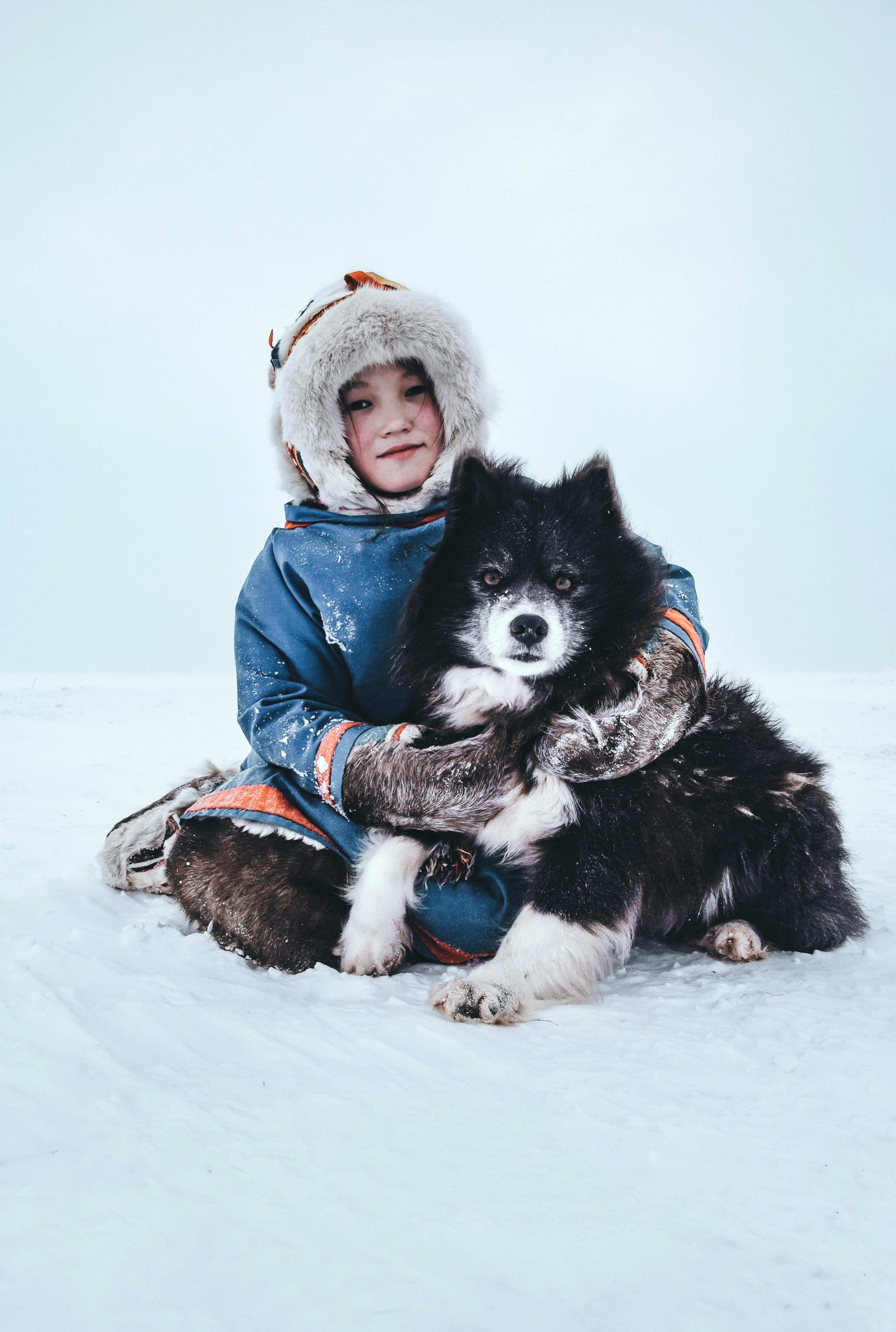 girl in winter coat sitting in snow hugging dog