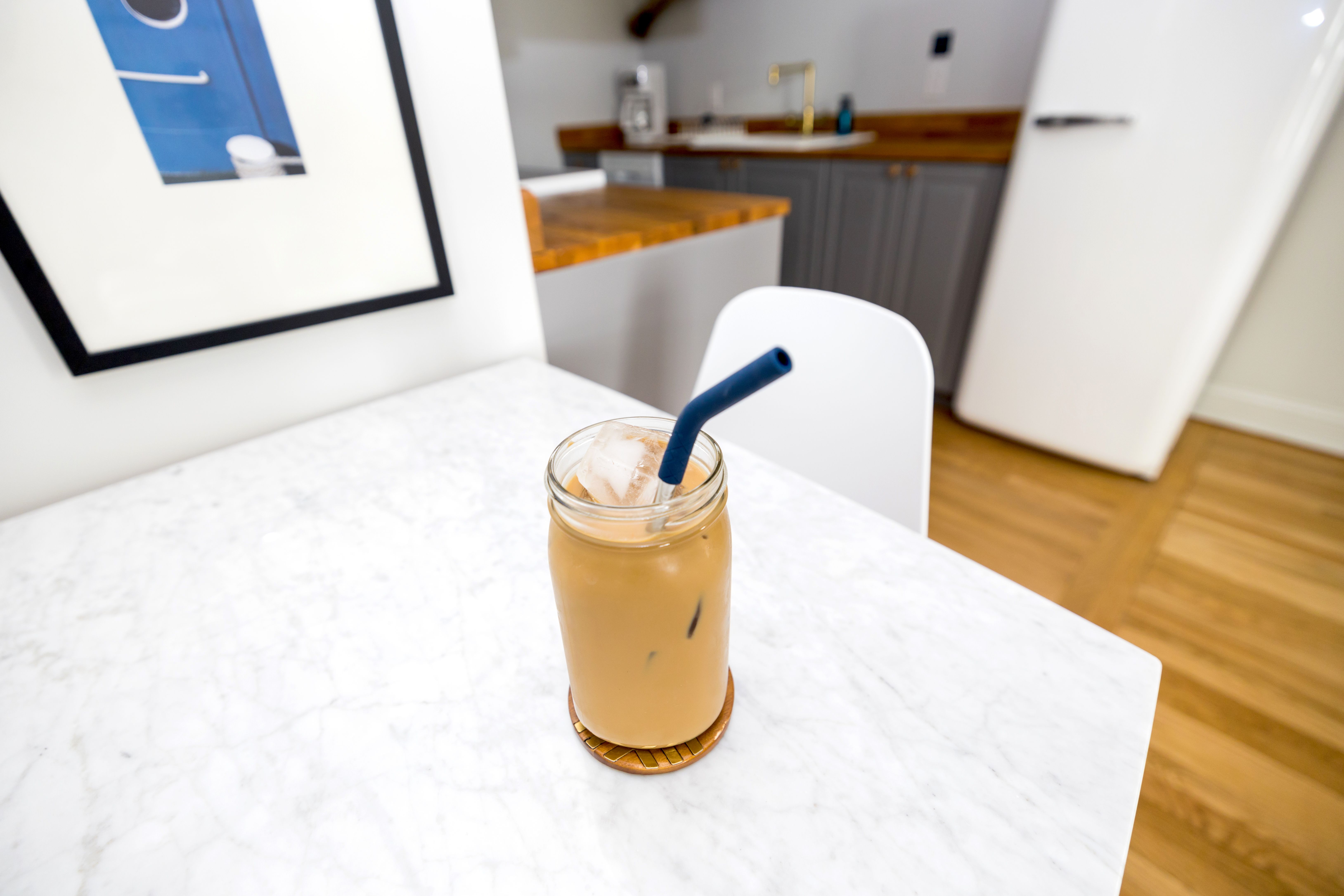 Glass of iced coffee with a straw on a marble table in a modern kitchen setting.