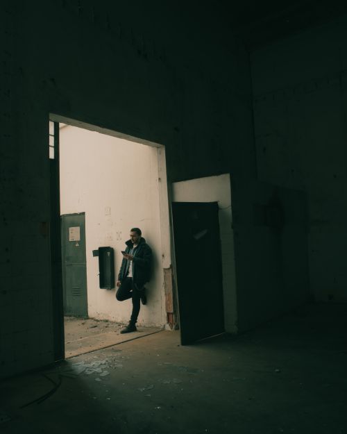 Free A man leans against a doorway in an abandoned building hallway, creating a dramatic moody atmosphere. Stock Photo