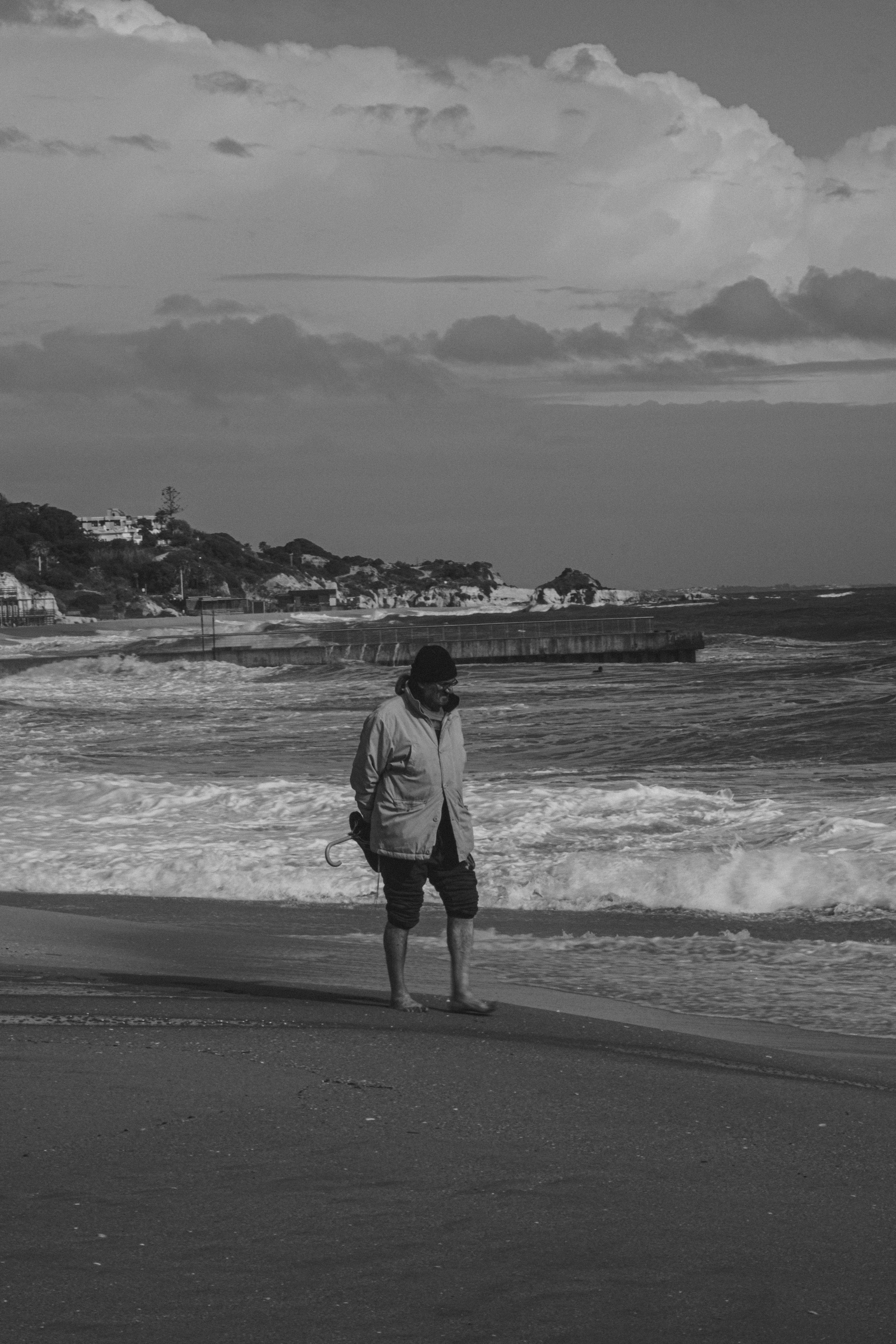 A solitary man walking along a serene beach captured in black and white, evoking solitude.