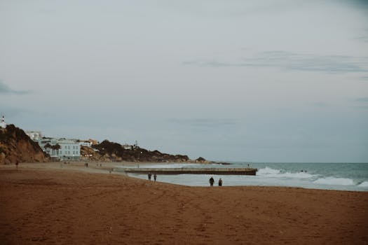 A tranquil scene of people walking along a sandy beach during a calm evening by the ocean.