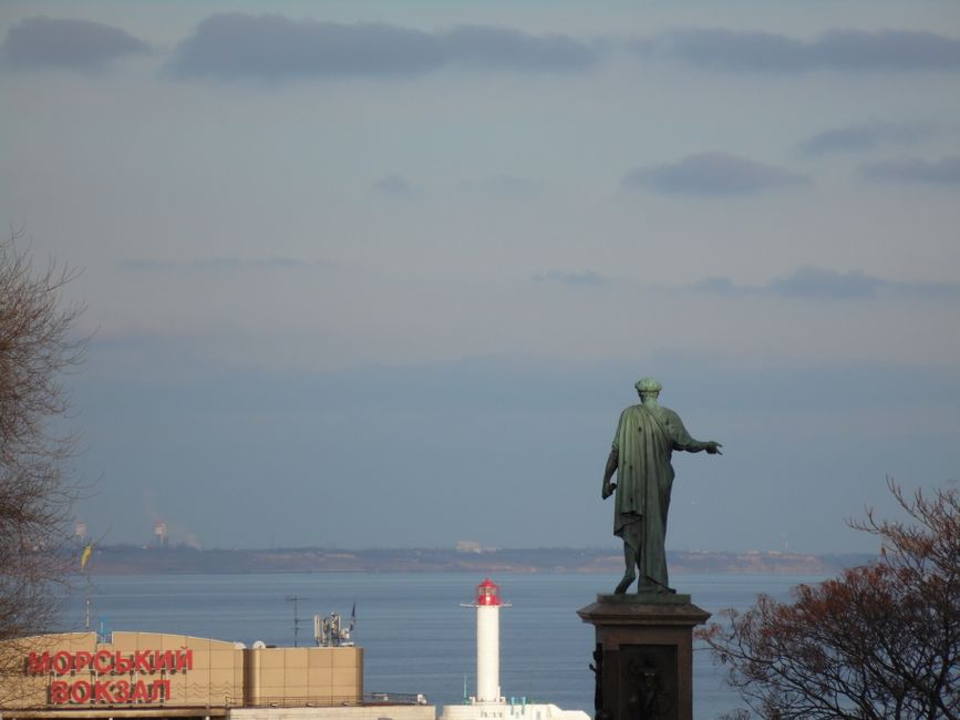A scenic view of a seaside statue overlooking a lighthouse in Odessa, Ukraine.