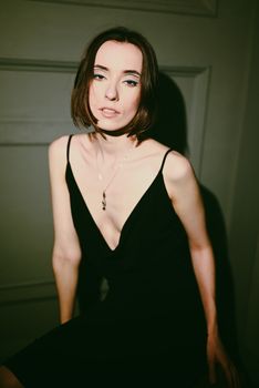 Stylish portrait of a young woman in a black dress and necklace in a studio setting.