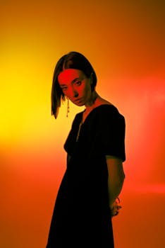 Artistic portrait of a woman in a black dress with vibrant orange background lighting.