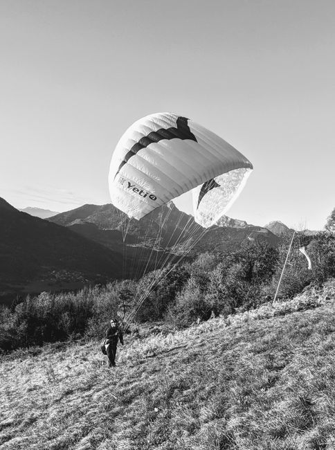 A black and white photo of a person paragliding in the mountains, capturing an adventurous spirit.