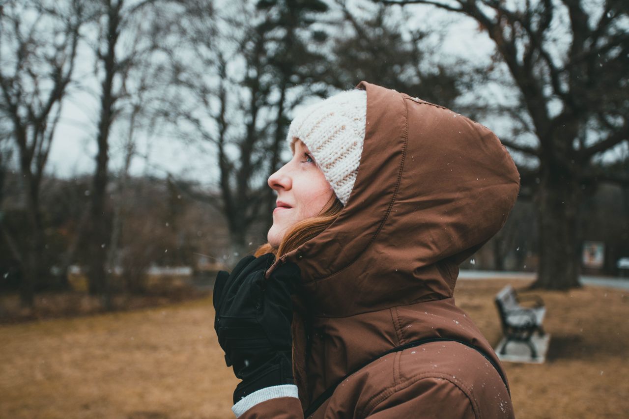Woman in a brown hooded coat in light snowfall at a park