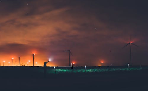 Фотография человека, держащего фонарик возле ветряных мельниц в ночное время