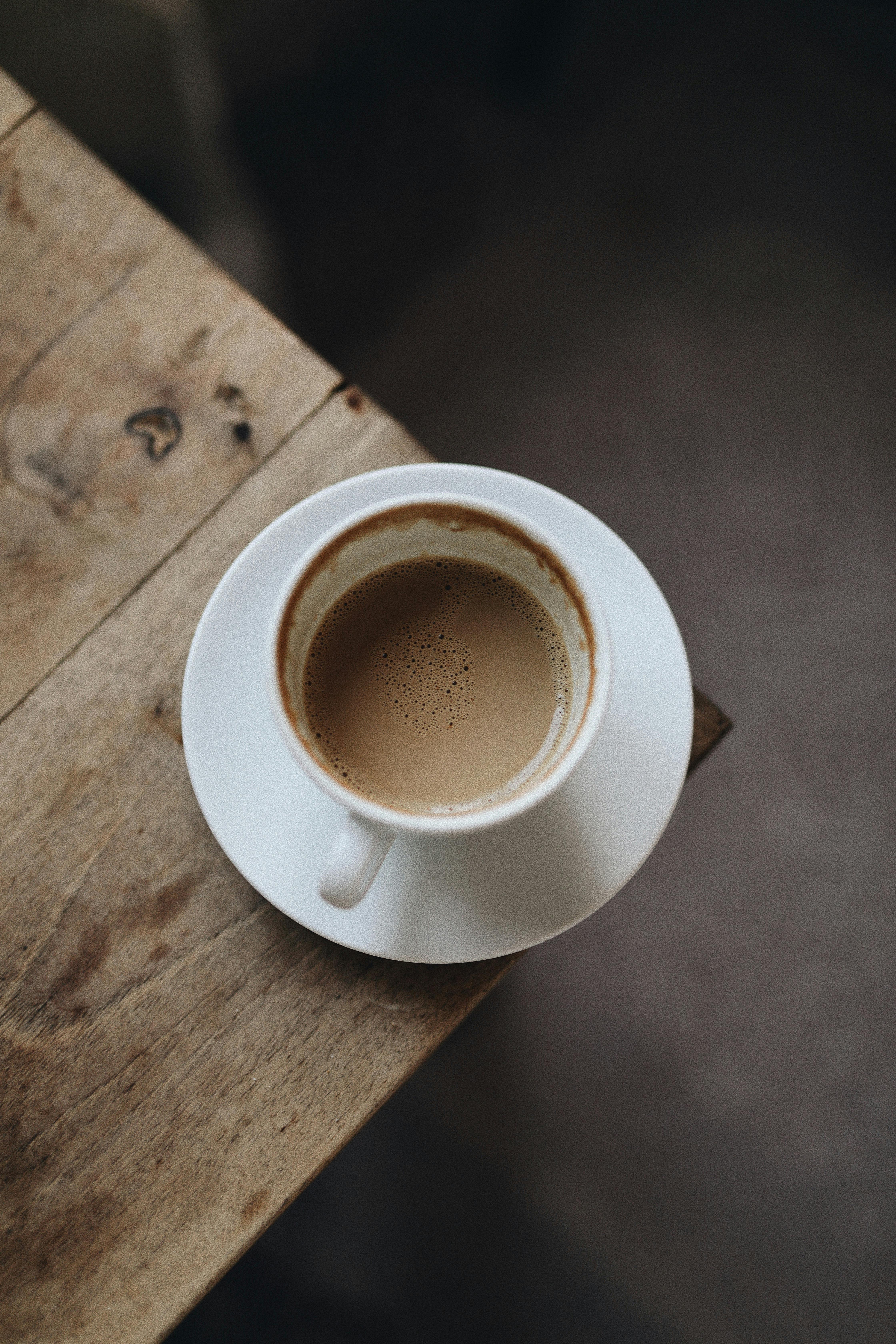 A minimalistic shot of coffee in a white cup on a rustic wooden surface, creating a warm and inviting atmosphere.