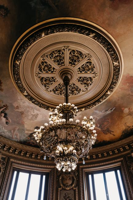 Lavish Baroque-style chandelier beneath an ornate painted ceiling in a Parisian interior.