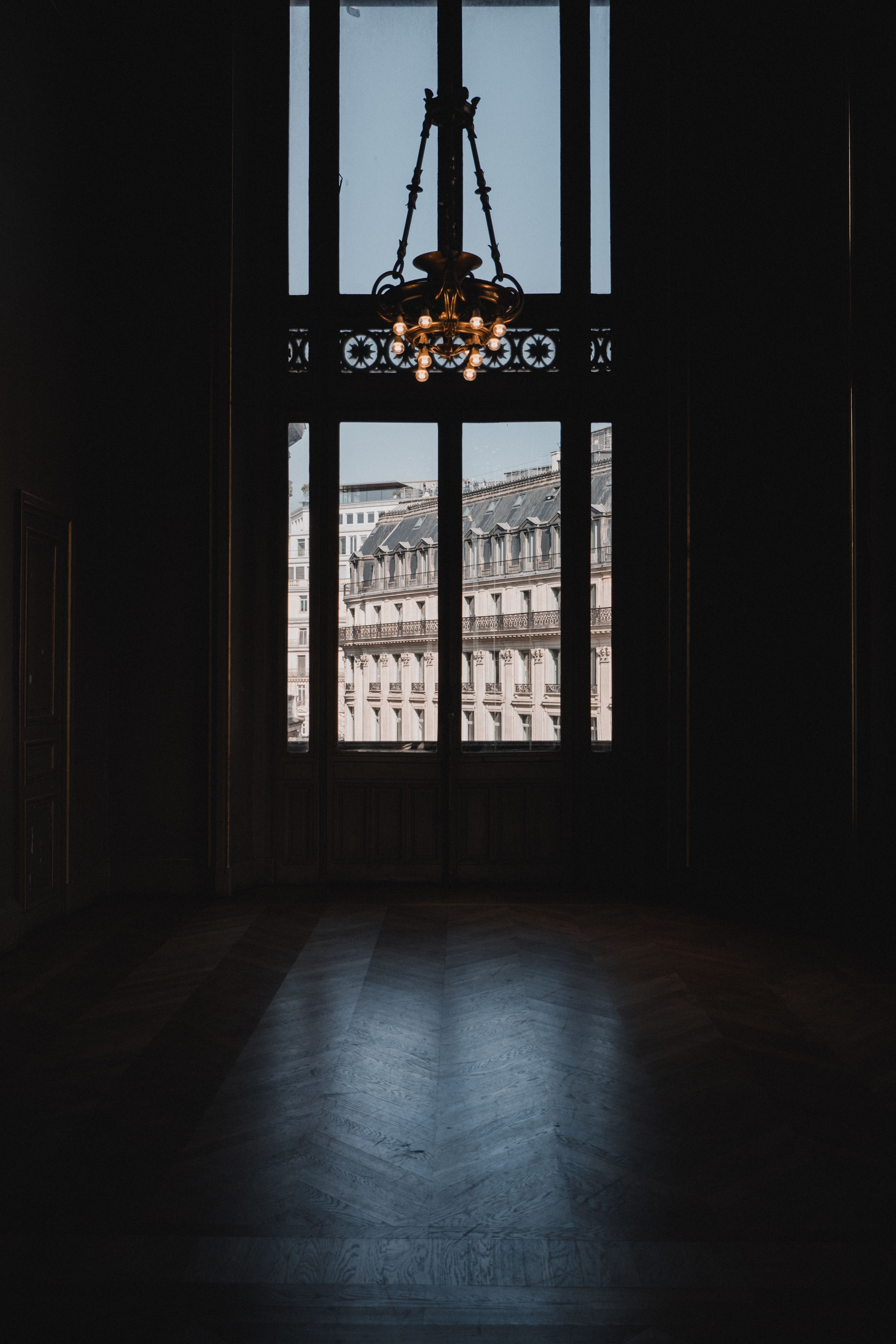 Elegant Parisian interior with chandelier, large windows, and view of historic architecture in Paris, France.