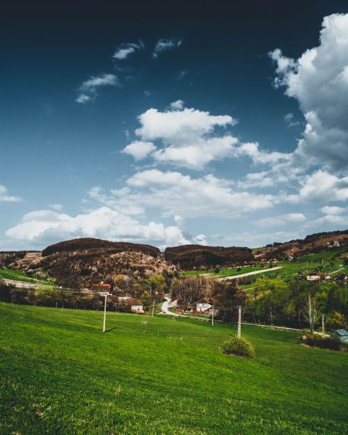 Free A serene countryside landscape with green fields, rolling hills, and a blue sky filled with clouds. Stock Photo