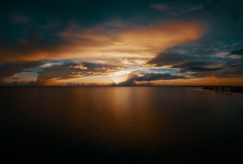 Free A breathtaking sunset over the ocean with dramatic clouds and warm colors reflecting on the water. Stock Photo