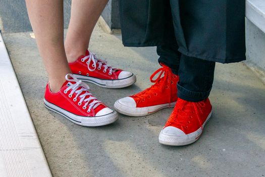 Two pairs of red sneakers on concrete, symbolizing casual fashion and friendship.