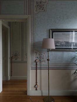 A sophisticated room featuring vintage wallpaper, framed art, and a stylish floor lamp.