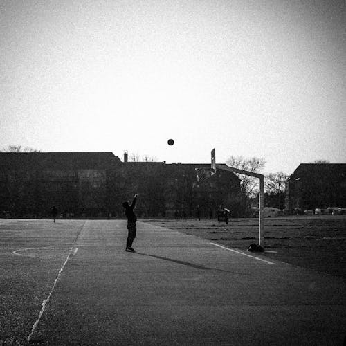Grayscale Photo of a Person Shooting a Basketball