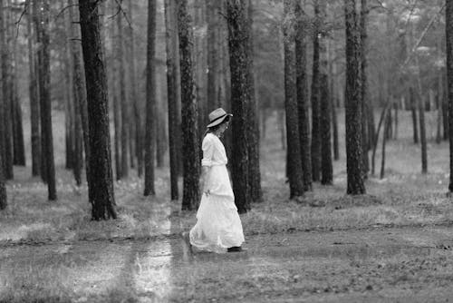 Grayscale Photo of Woman in White Dress Walking Near Trees