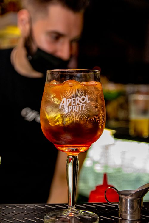 Free Close-up of a refreshing Aperol Spritz cocktail served at a bar in Pyrgi, Greece with a bartender in the background. Stock Photo