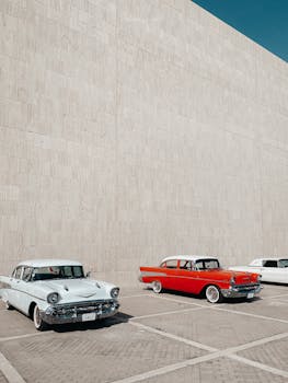 A lineup of vintage cars in a city setting under a clear blue sky.