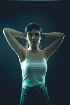 A confident young woman poses in a studio setting with dramatic backlighting and a dark backdrop.