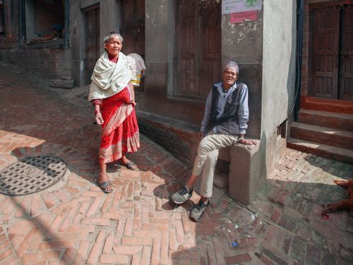 Free Elderly couple enjoying a sunny day on a rustic cobblestone street with traditional attire. Stock Photo