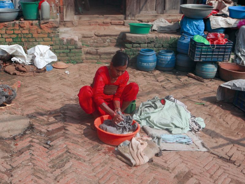 Woman in red traditional attire hand washing clothes outdoors on a sunny day