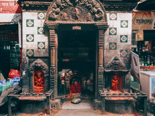 Free A small street shrine with detailed carvings and offerings in an urban setting. Stock Photo
