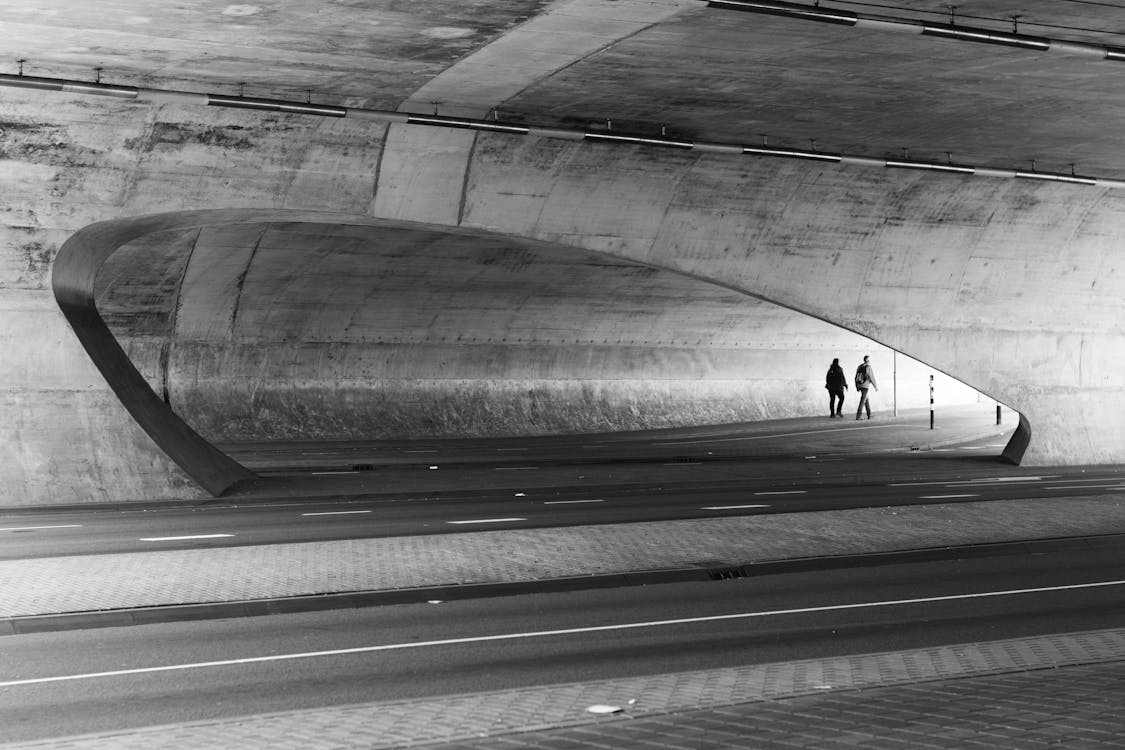 Greyscale Photography of Two People Walking Near Wall