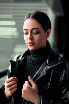 Portrait of a woman wearing a black leather jacket and turtleneck indoors, looking thoughtful.