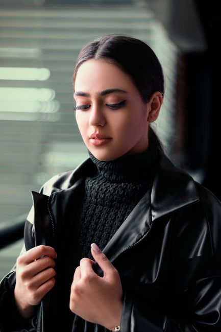 Portrait of a woman wearing a black leather jacket and turtleneck indoors, looking thoughtful.
