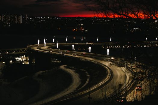 Aerial view of a beautifully illuminated curved bridge with city lights at twilight.
