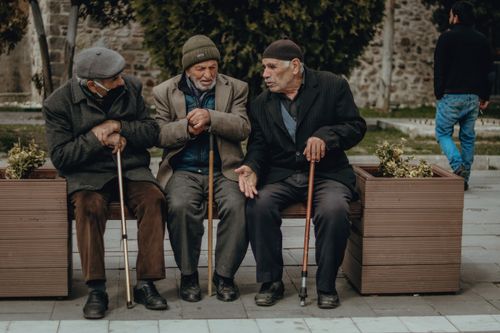 Free Three senior men in winter clothing having a discussion while sitting on a bench outdoors. Stock Photo