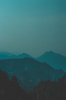 Serene view of misty blue mountains in Dhanolti, India at twilight, capturing nature's tranquility.