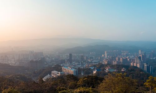 Free A stunning aerial view of a cityscape with mountains and trees during sunset. Stock Photo