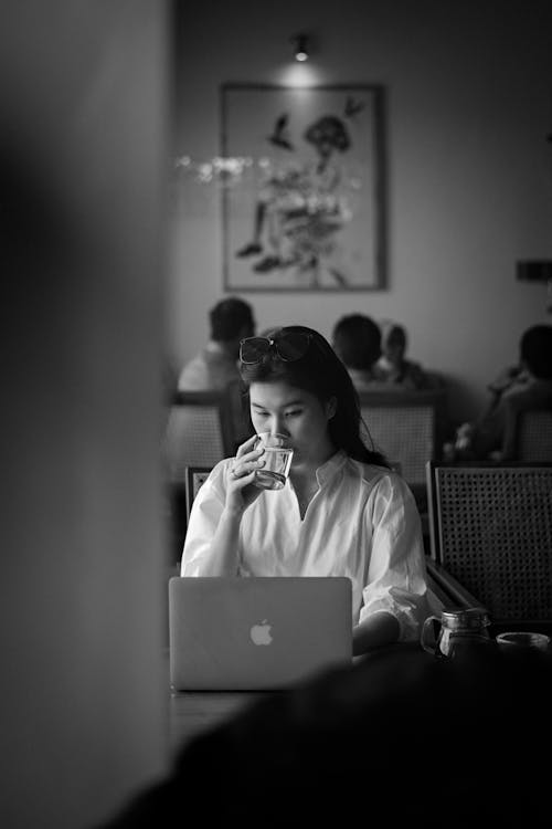 Grayscale Photo of Woman in White Long Sleeve Shirt Sitting at the Table