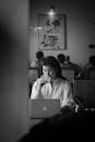 Grayscale Photo of Woman in White Long Sleeve Shirt Sitting at the Table