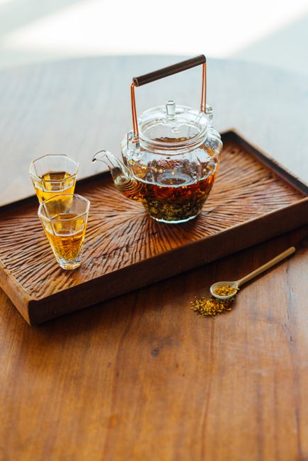 A glass teapot and cups with osmanthus tea on a wooden tray, bathed in warm sunlight.