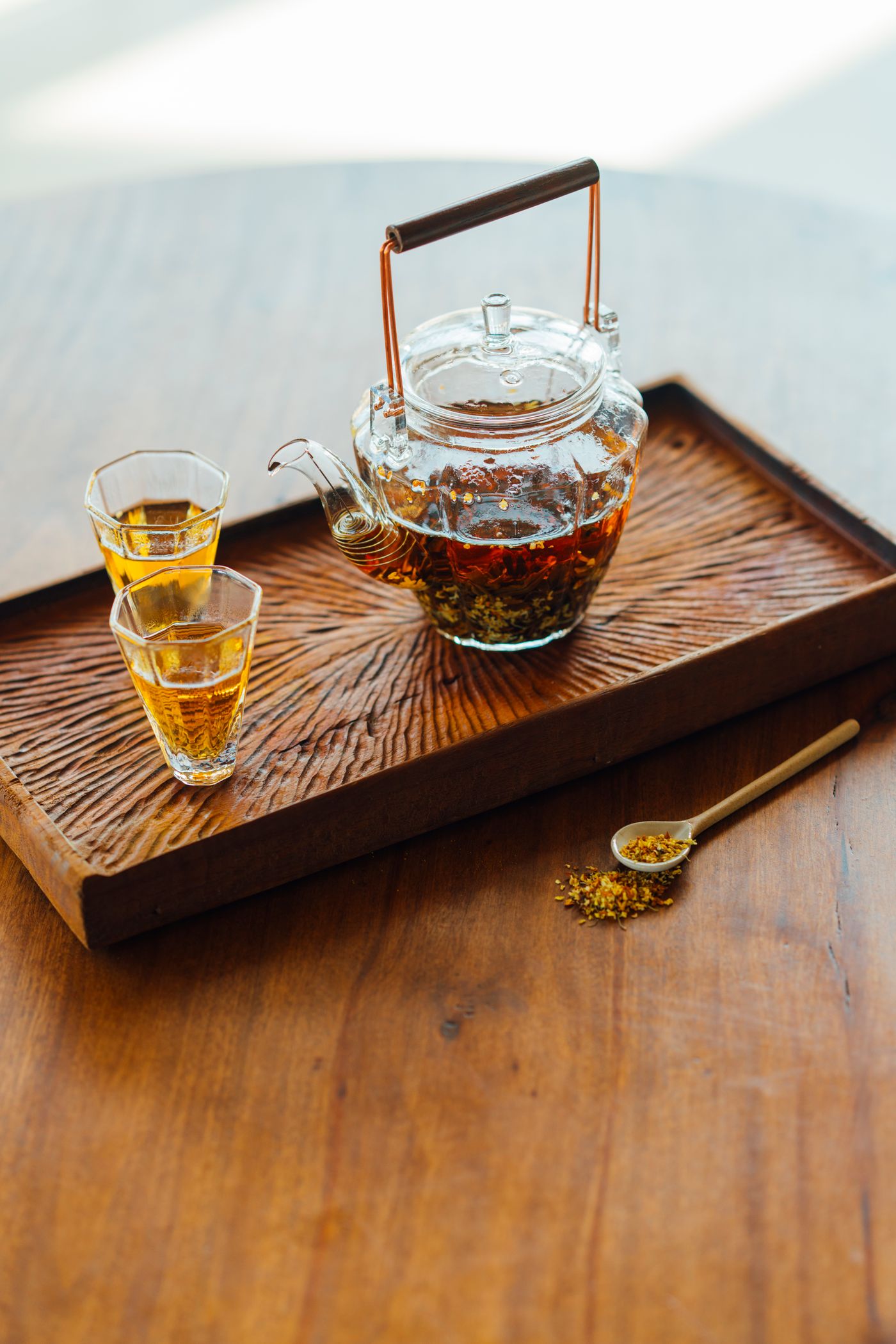 A glass teapot and cups with golden tea in warm sunlight.