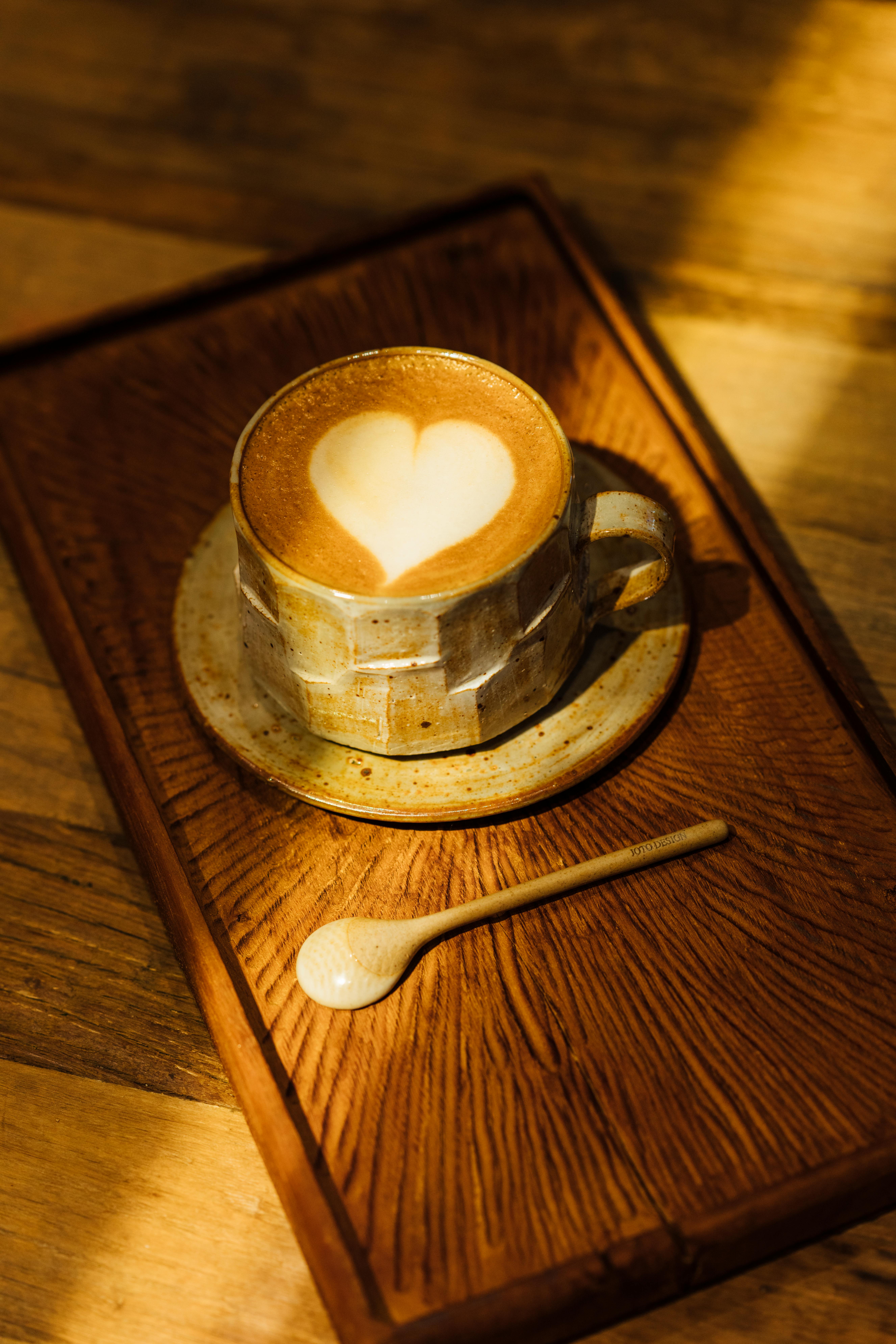 A rustic coffee cup with heart-shaped latte art on a wooden tray.