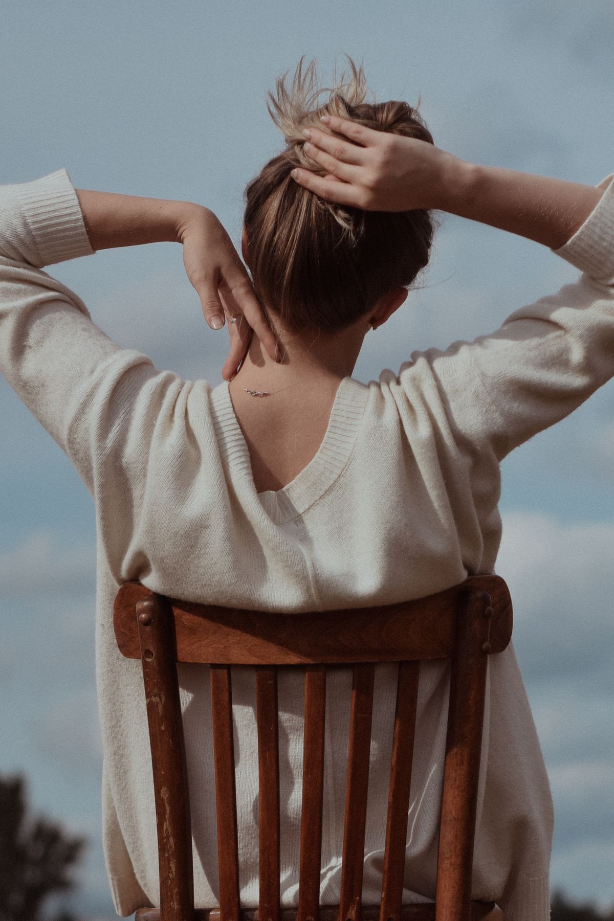 A woman in a white knit sweater sitting on a wooden chair — the fine summer sweater
